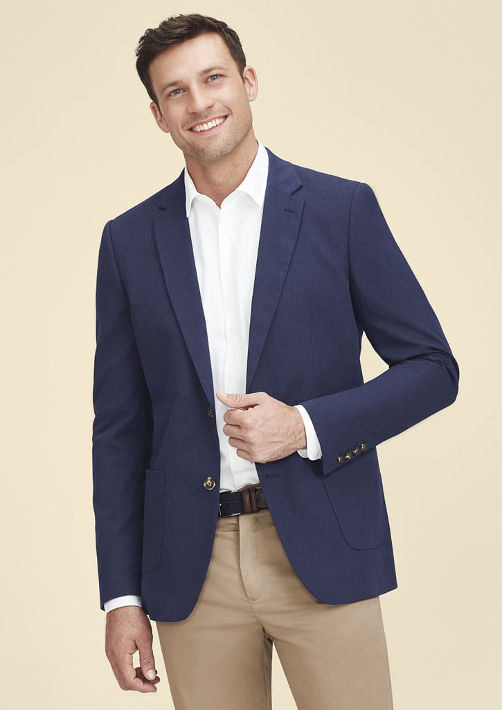 A man in a navy blazer over a white shirt, smiling against a neutral background. The blazer features a logo.
