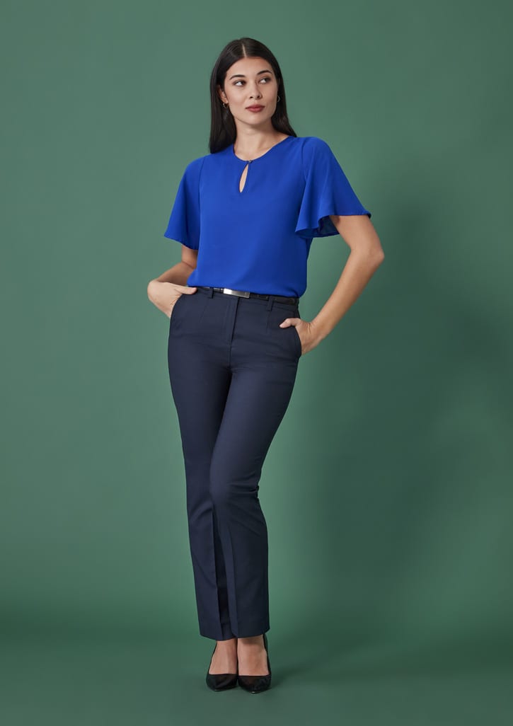 A model wearing navy tapered adjustable waist pants paired with a blue top against a green background.