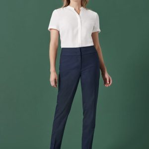 A woman wearing navy slim leg pants paired with a white blouse, standing against a green background.