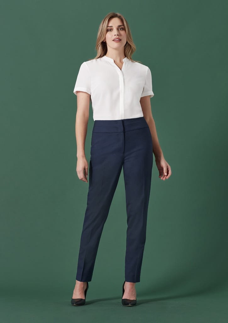 A woman wearing navy slim leg pants paired with a white blouse, standing against a green background.