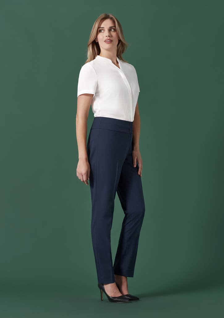 A woman wearing navy mid-waist slim leg pants paired with a white top, standing against a green background.