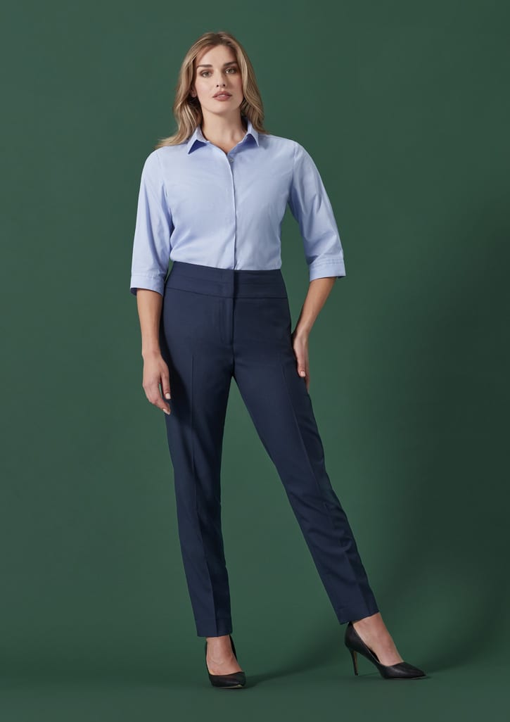 A model displays navy mid-waist slim leg pants paired with a light blue shirt against a green backdrop.
