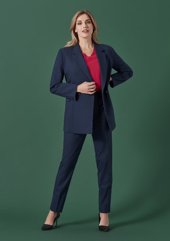 A woman wearing a navy blazer and matching slim leg pants, styled with a red top and black heels, against a green background.