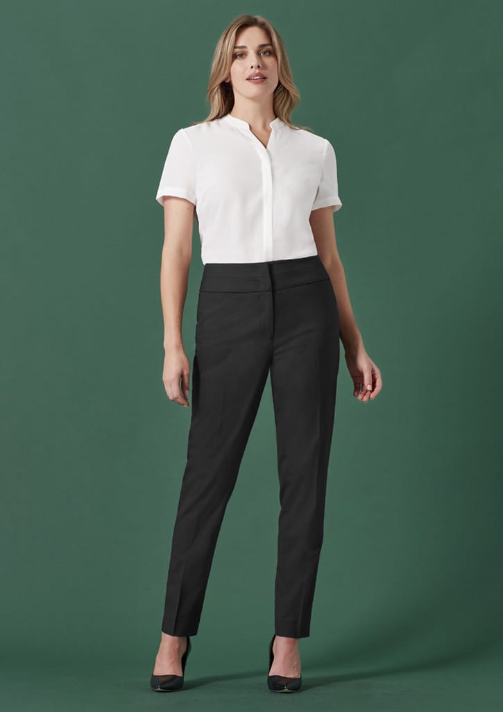 A pair of mid-waist slim leg pants in black, worn by a model with a white top against a green background.