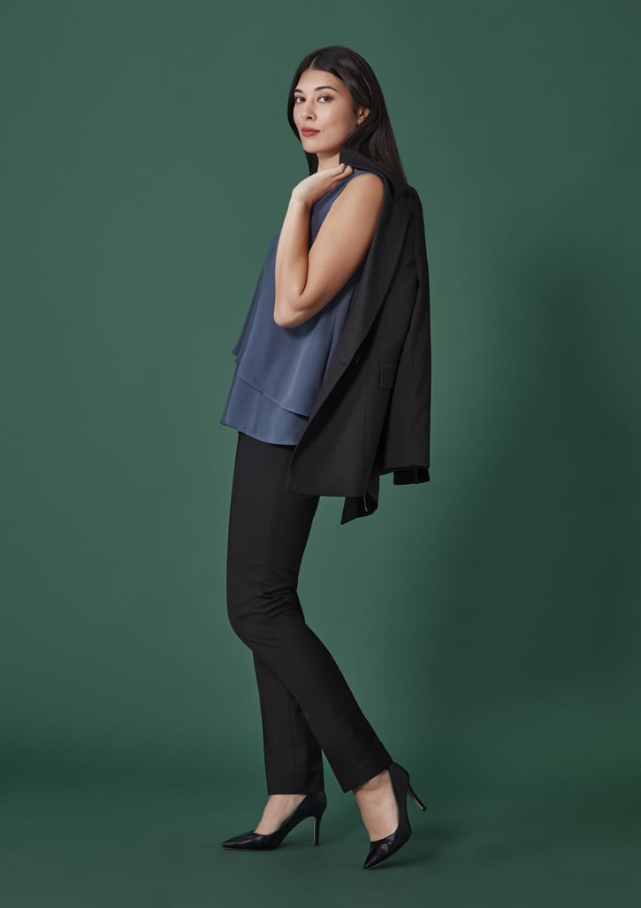 A model wearing black slim leg pants paired with a blue top and a black blazer on a green background.