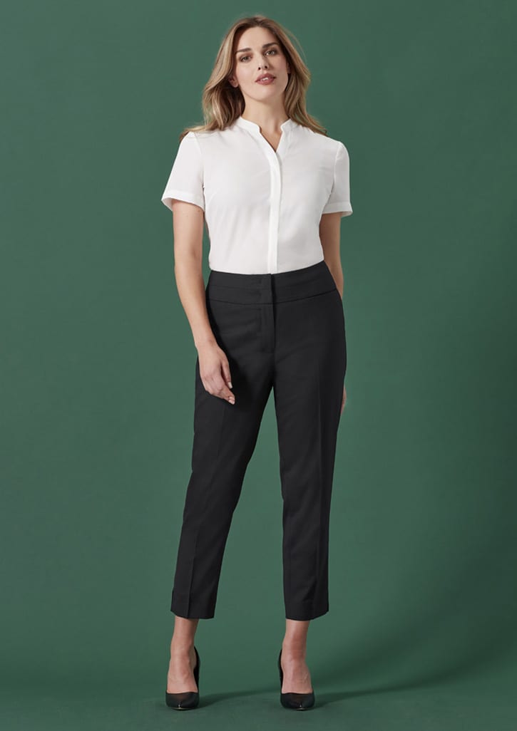 A mid-waist slim leg pant in black, paired with a white short-sleeve shirt. The model poses against a green background.