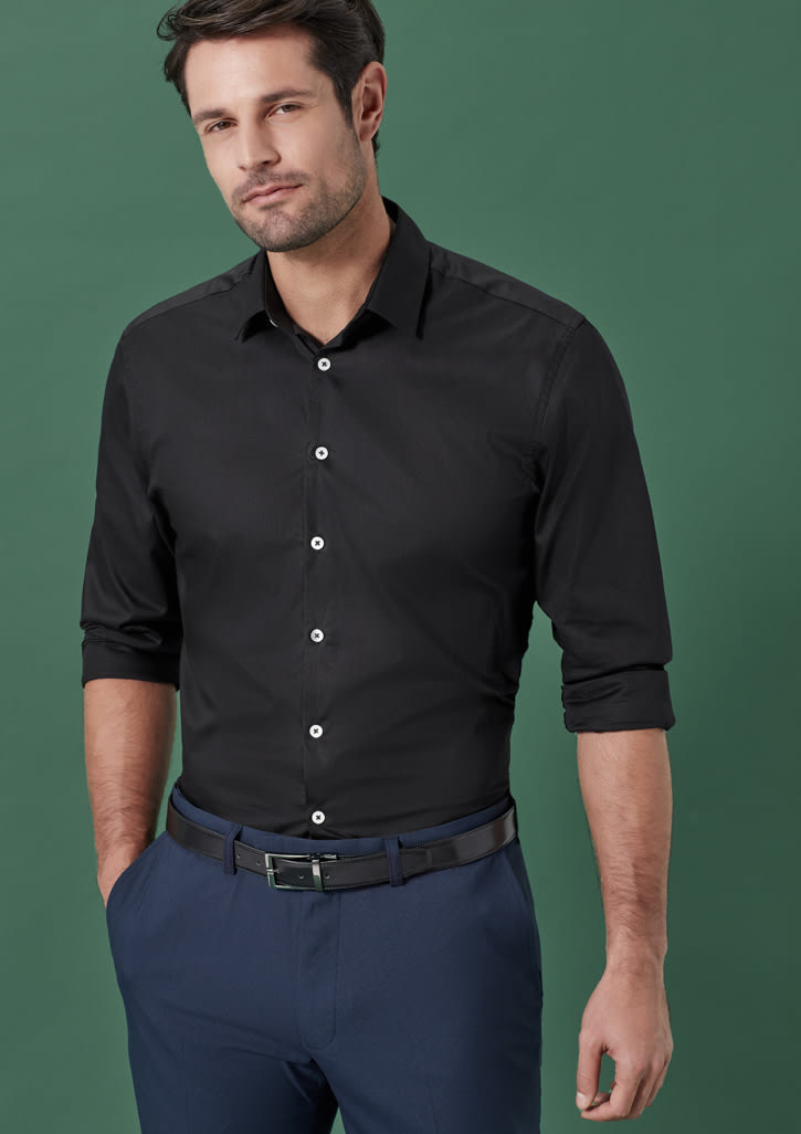 A man wearing a black button-up shirt and navy blue flat front pants, with a belt and a green background.