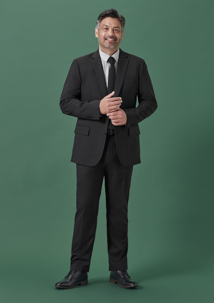 A man in a black suit and tie, standing confidently against a green background.