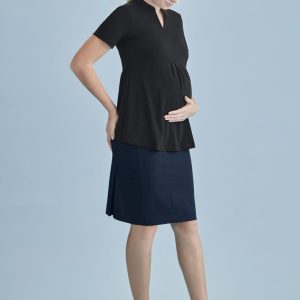 A pregnant woman wearing a black top and a navy maternity skirt, standing against a light blue background.