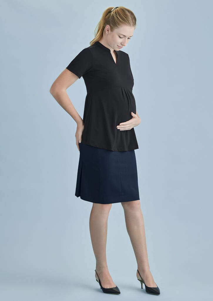 A pregnant woman wearing a black top and a navy maternity skirt, standing against a light blue background.