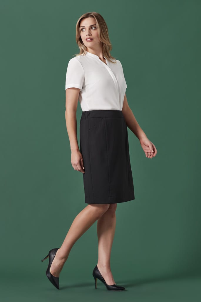 A woman wearing a white top and a black pencil skirt stands against a green background, showcasing the skirt's design.