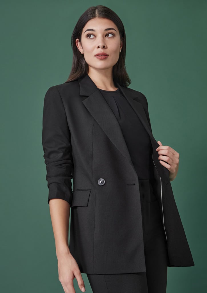 A black longline double-breasted women's jacket is styled with a shirt, set against a green background.