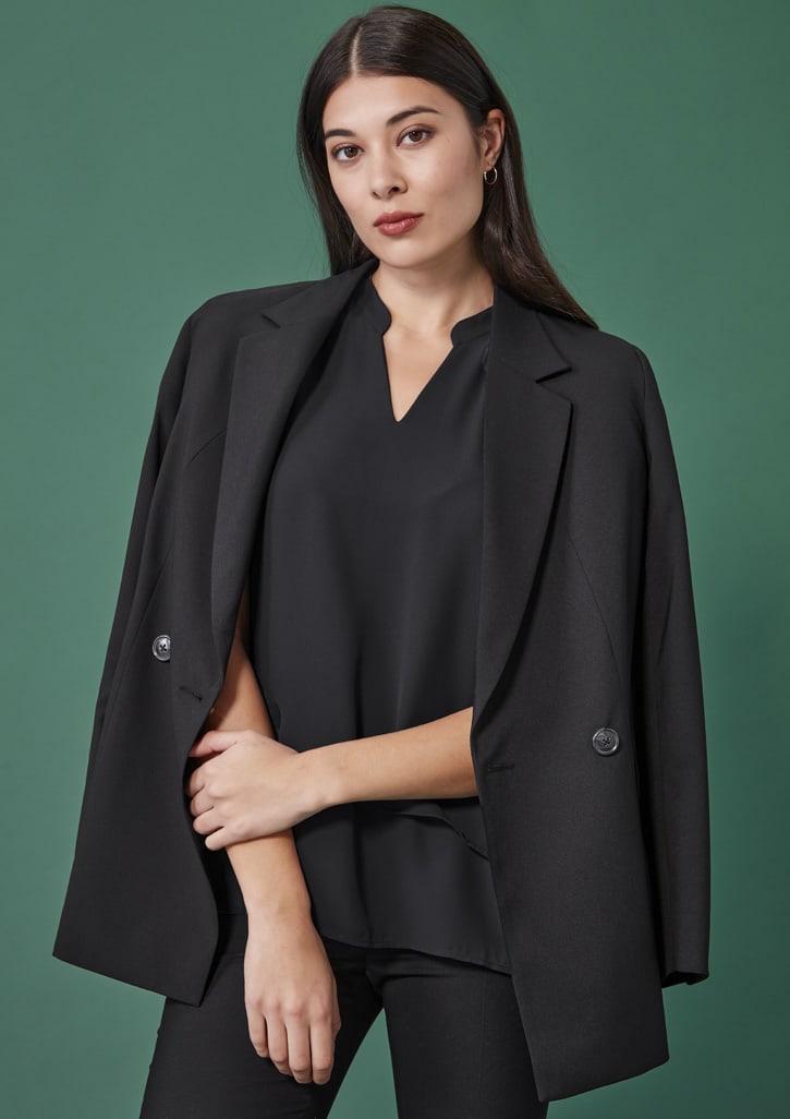 A black double-breasted longline jacket with an oversized fit, worn over a black top against a green background.