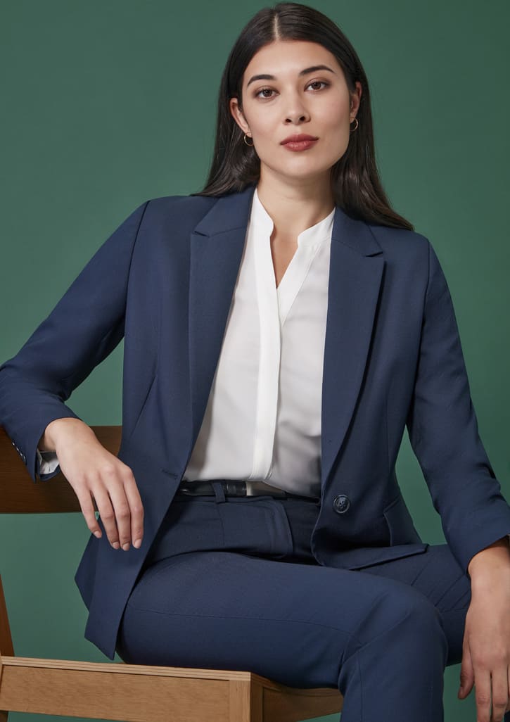 A navy mid-length blazer with a single button, worn over a white blouse, displayed against a green background.