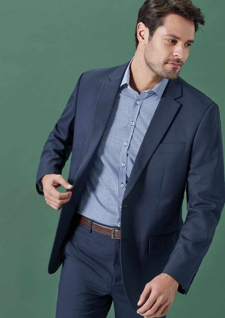 A man in a navy blue suit jacket, featuring a pocket, paired with a light striped shirt against a green background.