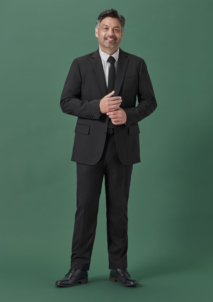 A black suit jacket worn by a man, paired with a white shirt and black tie, standing against a green background.