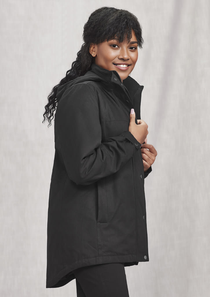 A black women's comfort jacket with a high collar and pockets, featuring a logo. Model is smiling and posed.