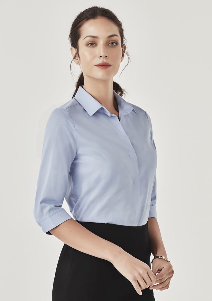 A light blue women's button-up shirt with three-quarter sleeves and a collar, featuring a subtle branding logo.