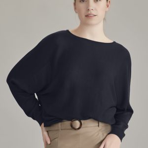 A black batwing sweater top worn by a model, paired with a beige skirt, showcasing relaxed fit and casual style.