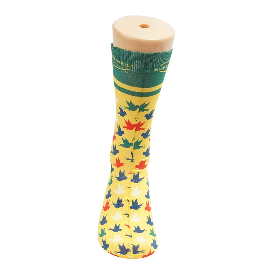 Bright yellow socks featuring a multicoloured leaf pattern, displayed on a sock model. Contains a logo.