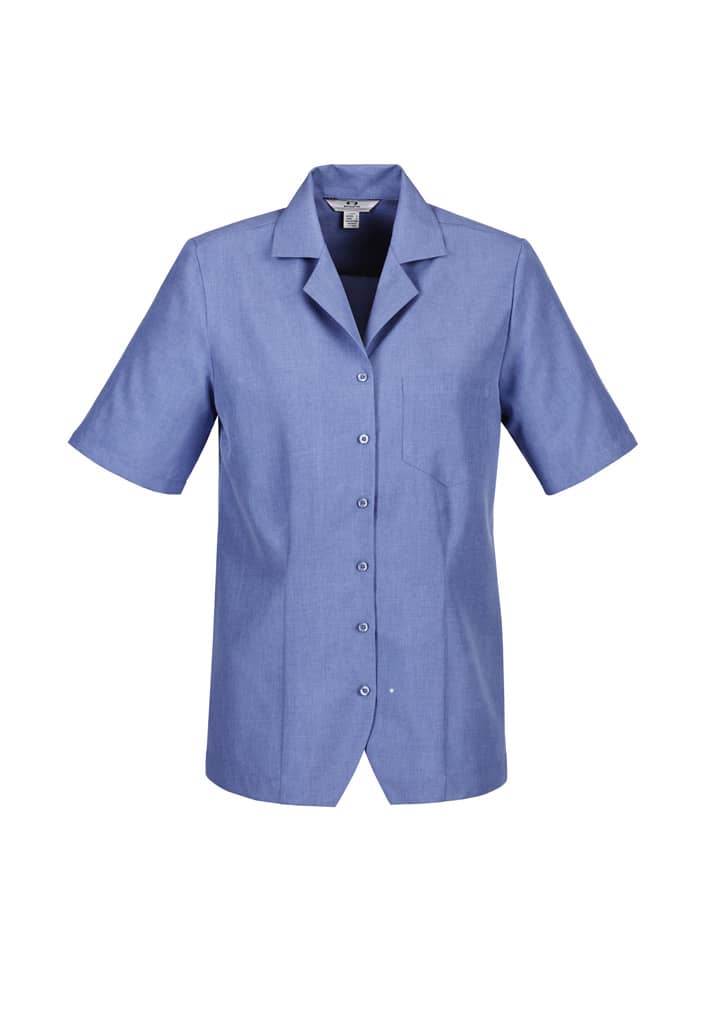 A blue overblouse with short sleeves, featuring a collar and a pocket. The garment has buttons down the front and includes a logo.