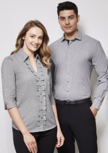 A woman and man wearing matching black and white button-up shirts, featuring a ruffled design and tailored fit.