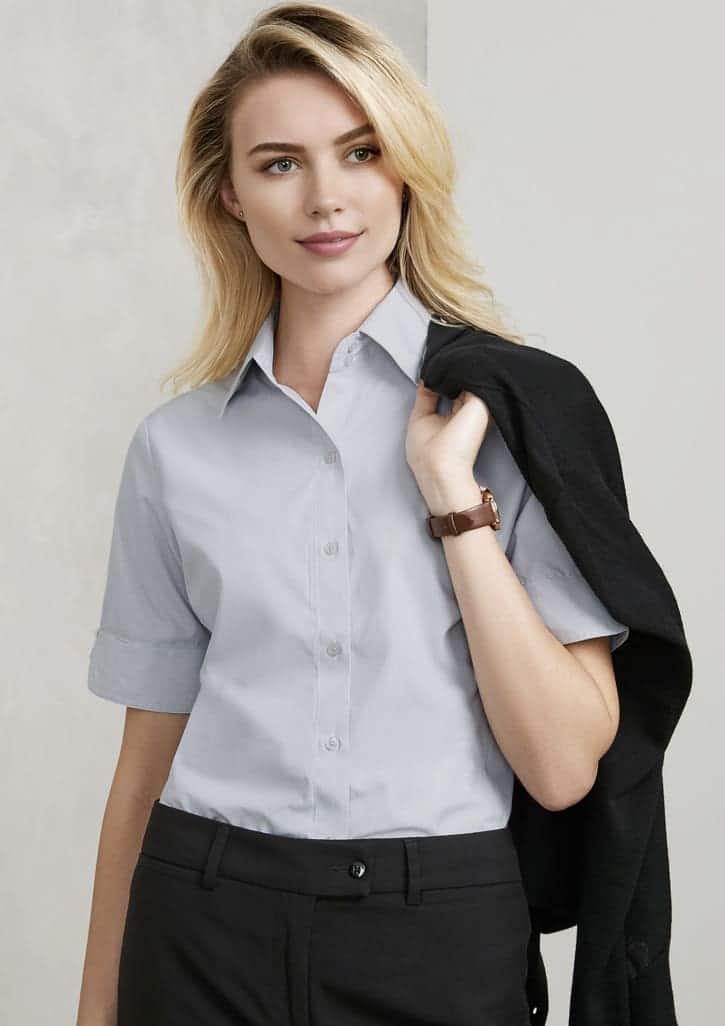 A light grey short sleeve button-up shirt featuring a classic collar, paired with black trousers. It has a logo branding.
