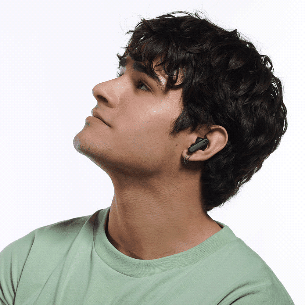 A person wearing black Skullcandy Smokin' Buds earbuds, looking upwards against a plain background.
