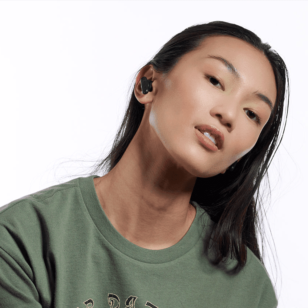 A model wearing black Skullcandy Smokin' Buds earbuds, styled in a green sweatshirt against a white background.