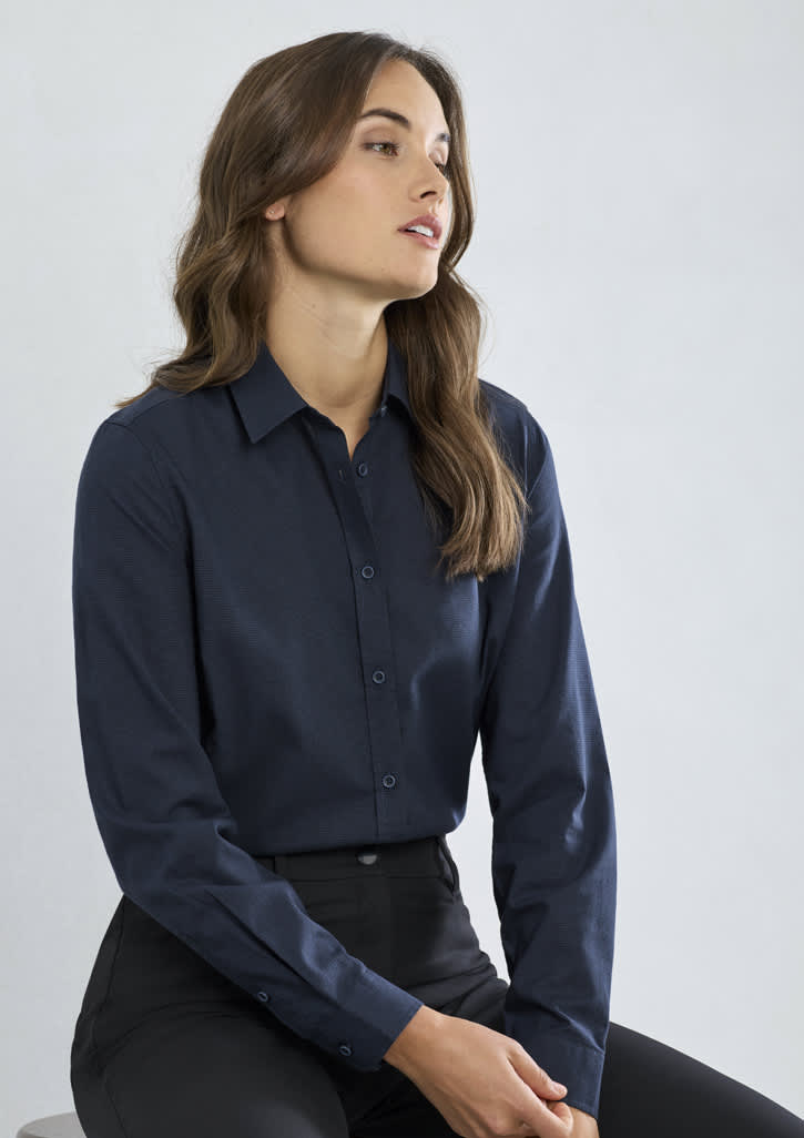 A woman in a navy long sleeve button-up shirt, seated against a light background, paired with black trousers.
