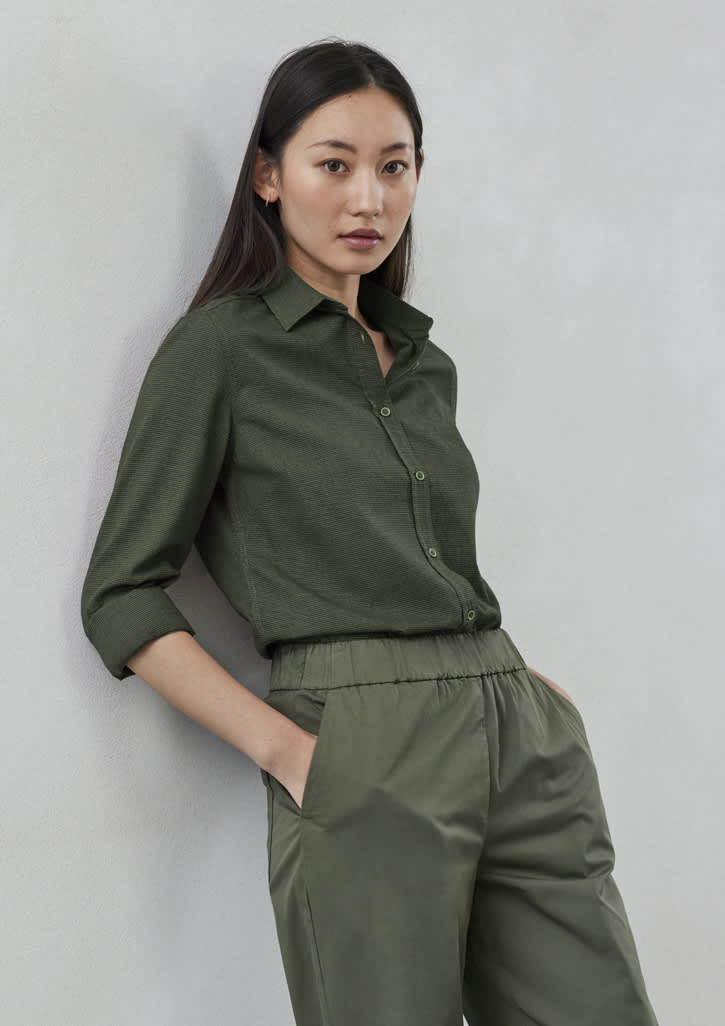 A green long sleeve button-up shirt is worn with matching trousers, displayed against a light background.