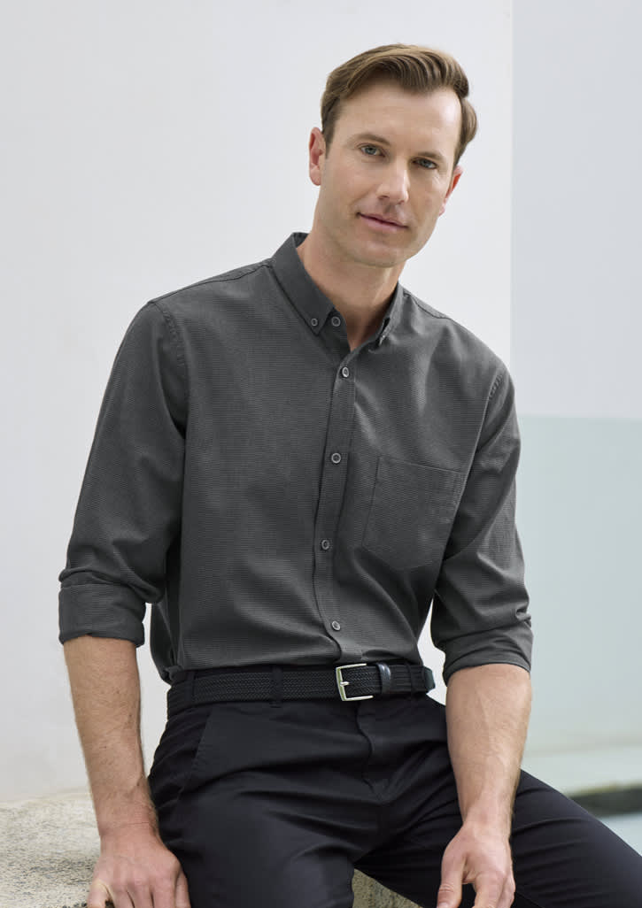 A long sleeve button-up shirt in charcoal grey, featuring a pocket and a branded logo, modelled by a man.
