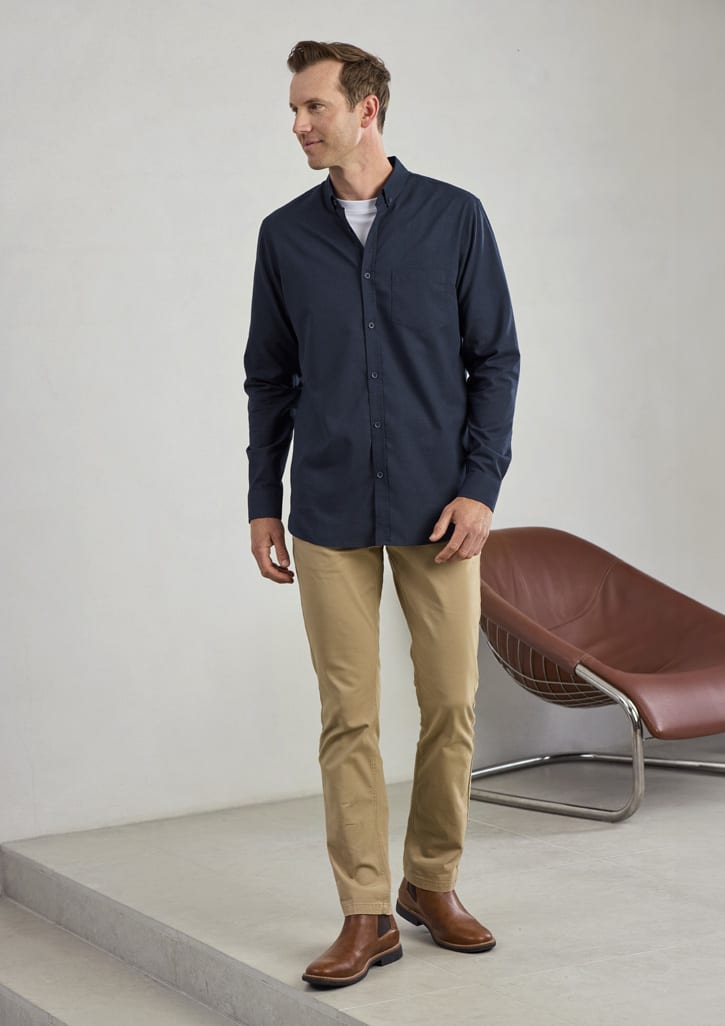 A long sleeve button-up shirt in navy, paired with beige trousers and brown boots, displayed in a minimalist setting.