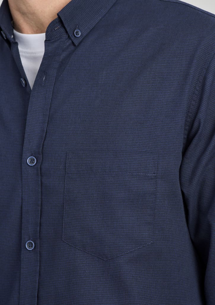 A navy blue long sleeve button-up shirt featuring a single chest pocket and a collar, complete with branding.