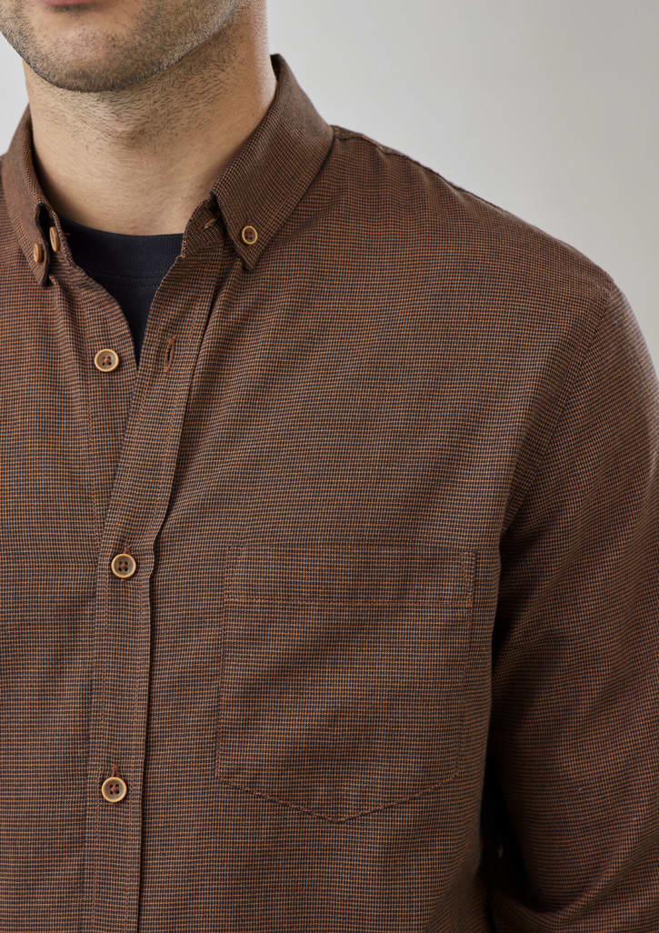 A brown button-up long sleeve shirt featuring a check pattern and a chest pocket. It has a logo on the label.
