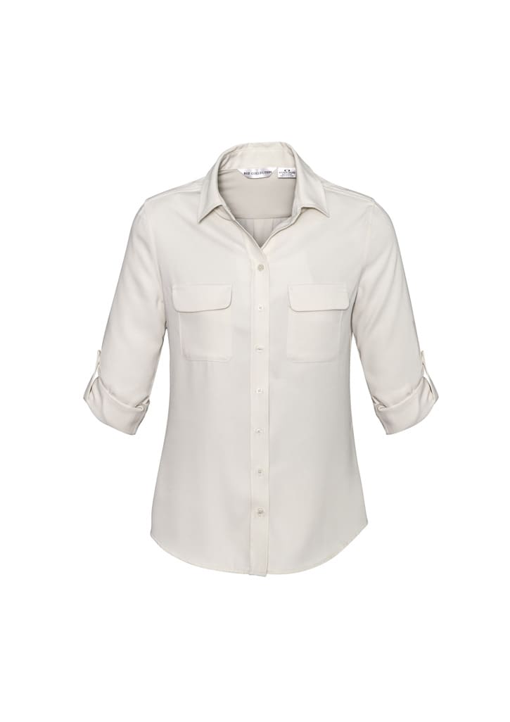 A women's long sleeve button-up shirt in cream, featuring two front pockets and rolled-up sleeves. It has a logo.