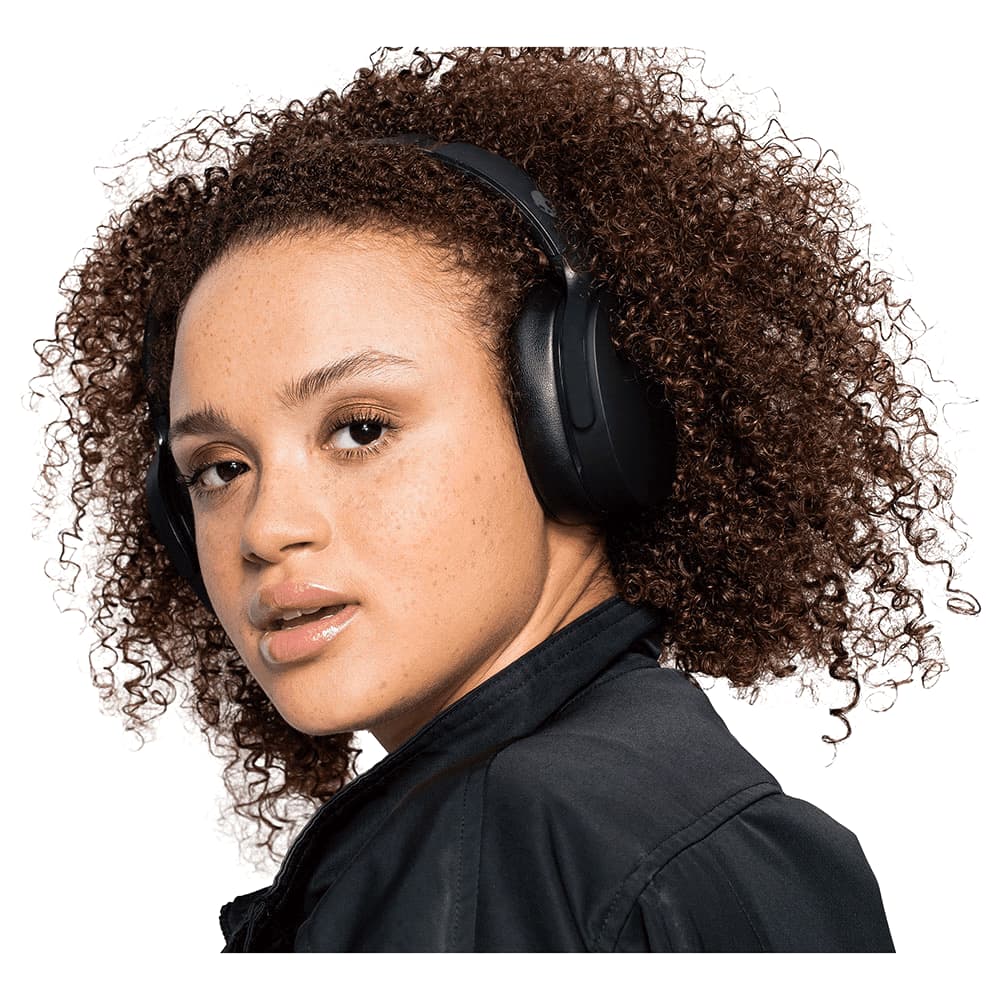 A woman wearing a black and white jacket and patterned leggings, listening to headphones. The product features a logo.