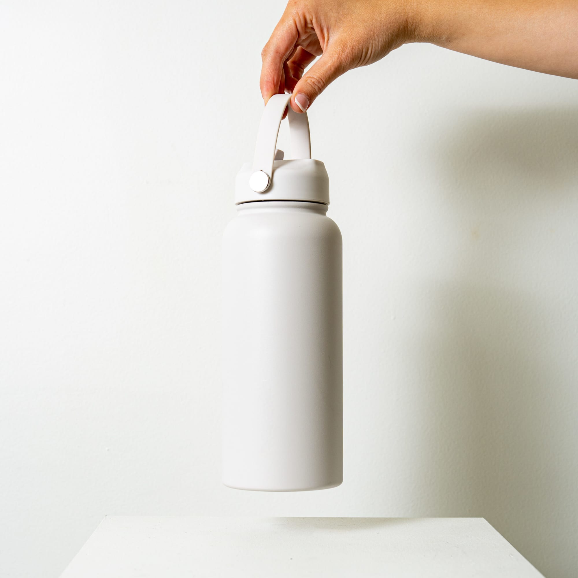 A drink bottle in soft white, featuring a sturdy handle and a sleek design. It has a logo on the front.
