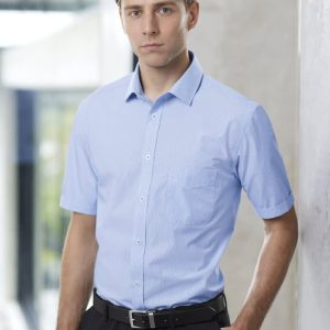 A light blue short sleeve button-up shirt on a model, featuring a chest pocket and a logo.
