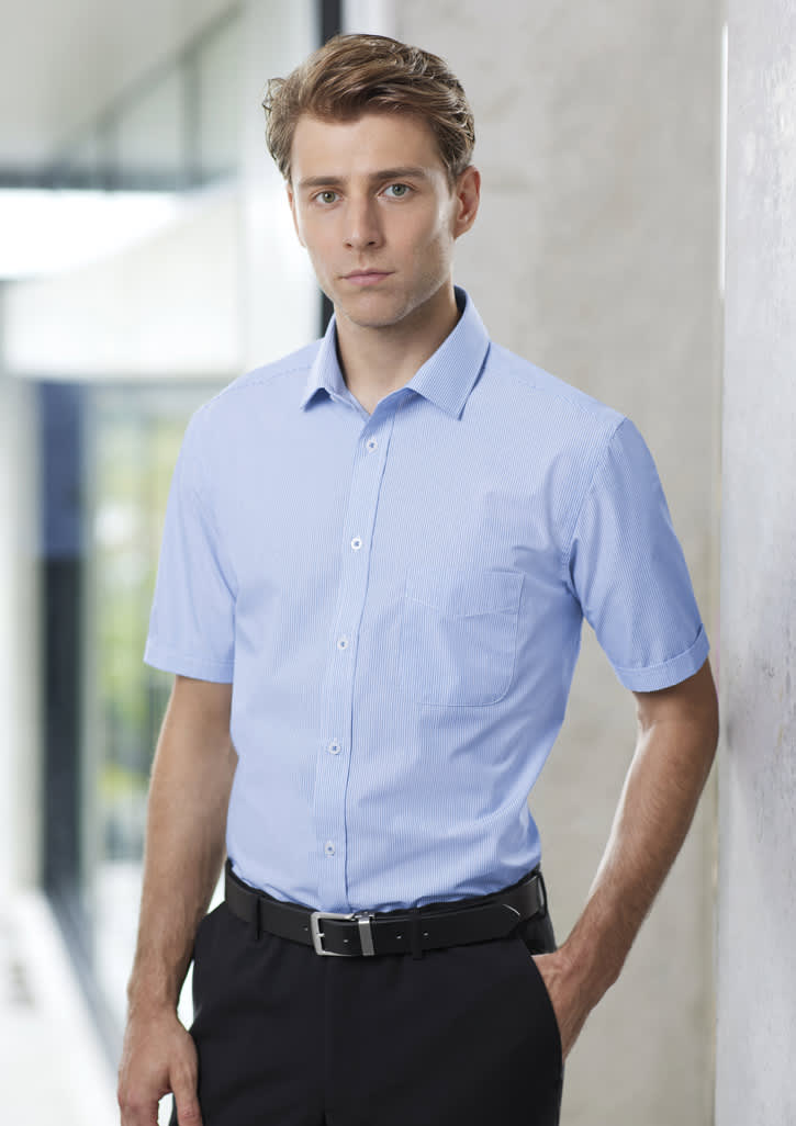A light blue short sleeve button-up shirt on a model, featuring a chest pocket and a logo.