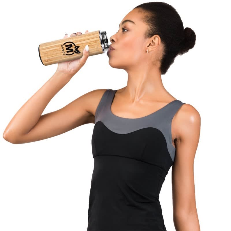A drink bottle with a bamboo exterior and stainless steel interior, held by a person in activewear.