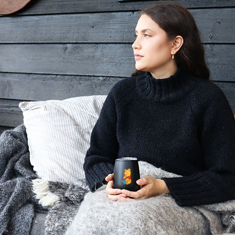 A drink mug with a Zen mirror finish in black, featuring a design, held by a person seated on a couch with cushions.