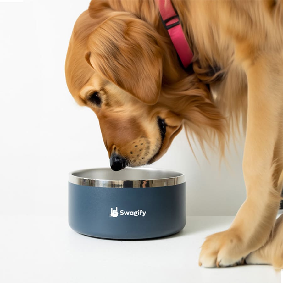 A dog leaning over a stainless steel, navy blue pet bowl with a logo on the front.