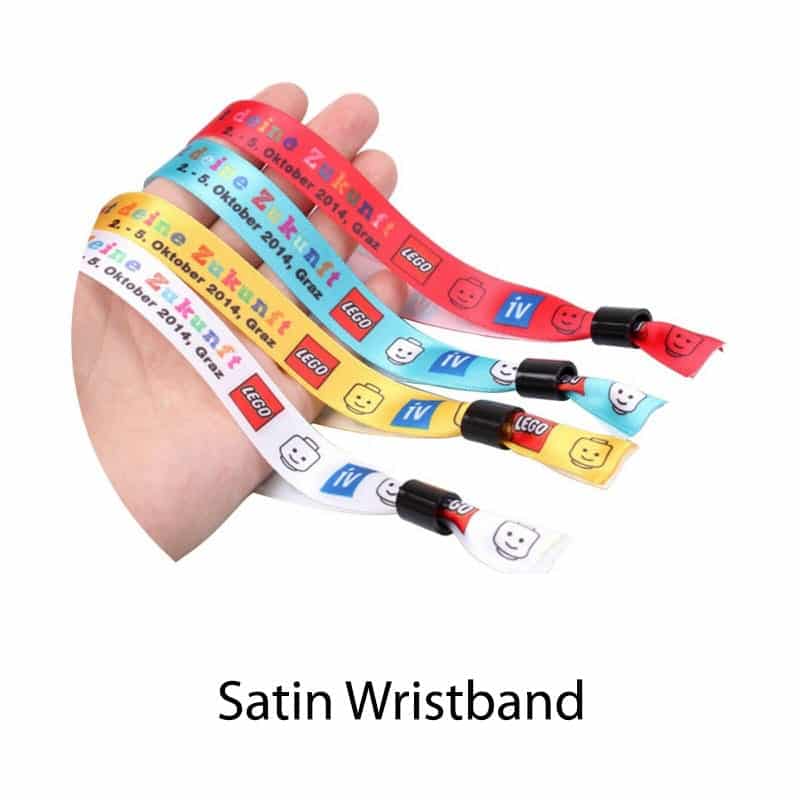 A hand holding several satin wristbands in red, yellow, blue, and light blue, featuring various colourful designs.