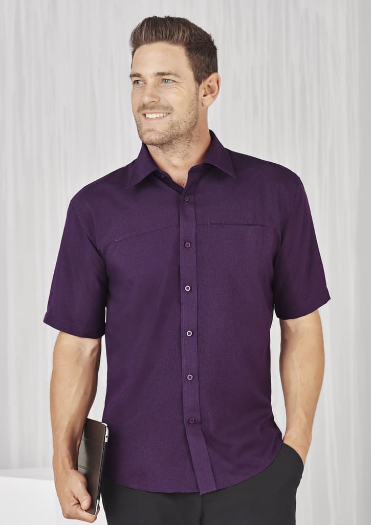 A plain short sleeve shirt in a rich purple colour with a button-up front and a pocket, featuring a logo.
