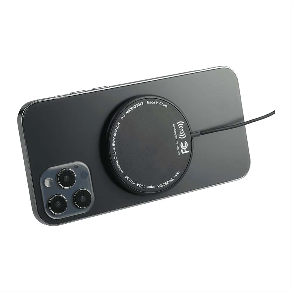 A round black wireless charging pad placed on the back of a smartphone. The pad has a logo.