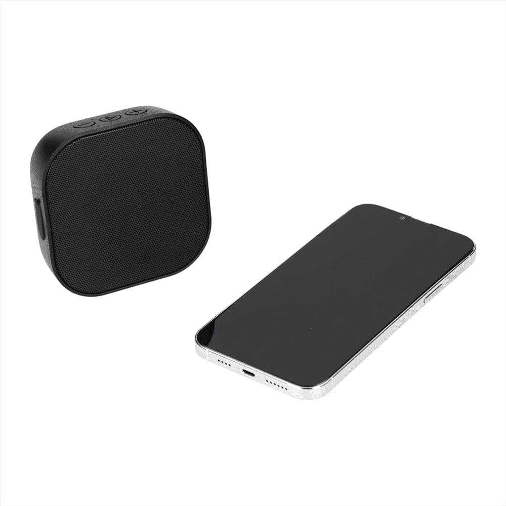 A black Bluetooth speaker beside a sleek smartphone, featuring a minimalist design and a logo.