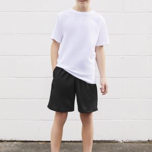A young boy poses in a white t-shirt paired with black sports shorts, standing against a white wall.