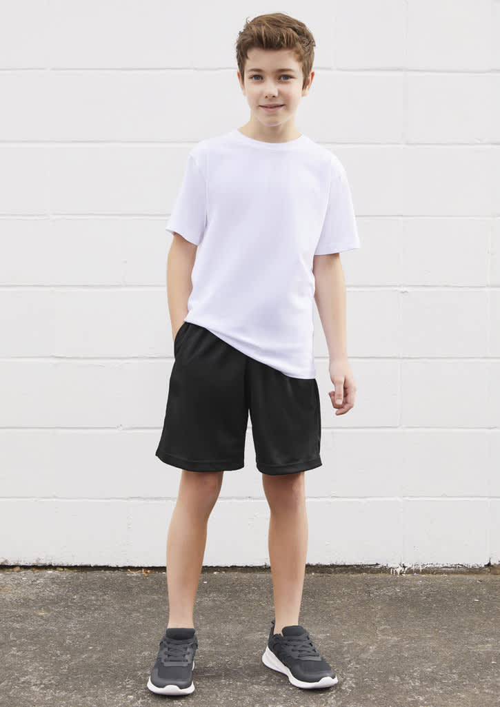 A young boy poses in a white t-shirt paired with black sports shorts, standing against a white wall.