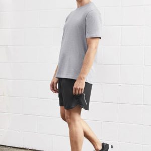A man stands wearing grey sports shorts and a matching grey t-shirt, with black athletic shoes. The backdrop is white.